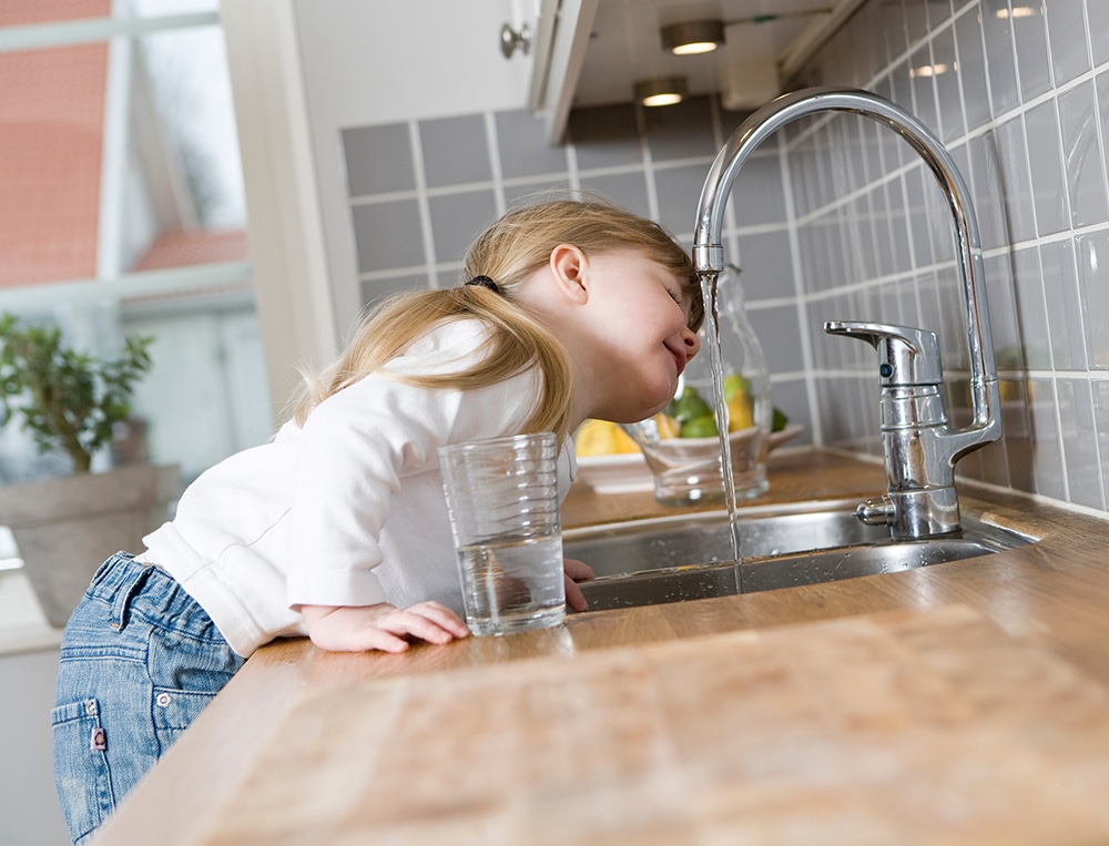 Petite fille boit au robinet de l'eau potable avec l'adoucisseur d'eau